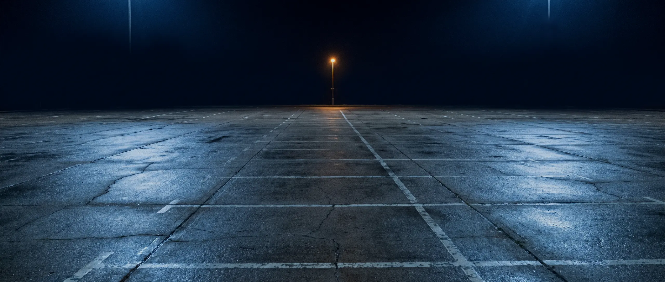 Parking d’entreprise vide la nuit, béton mouillé et marquage au sol