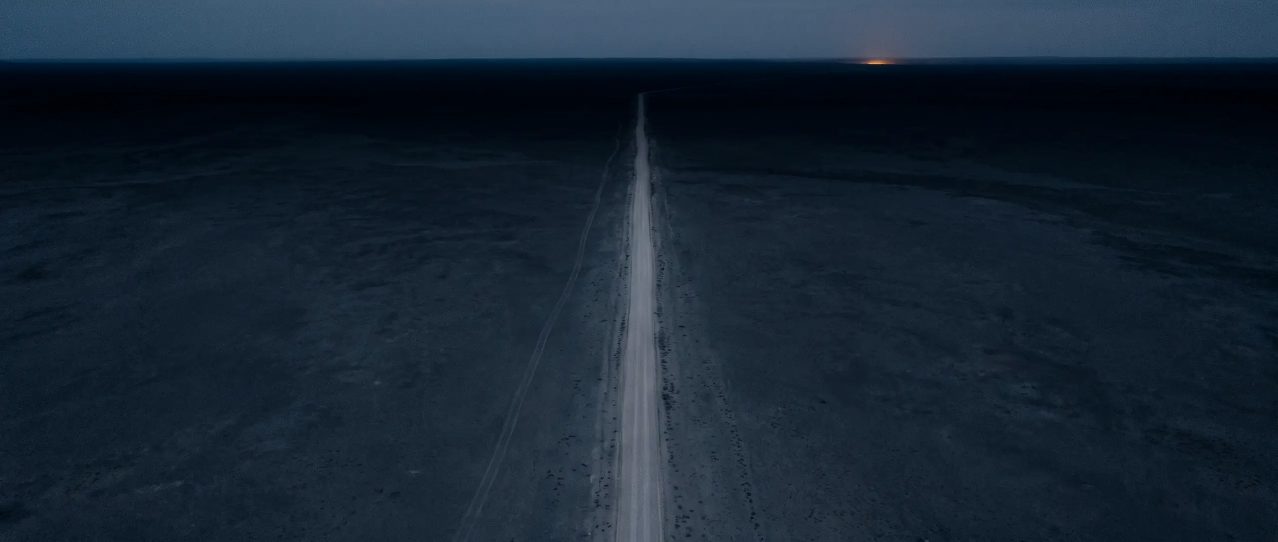 Plateau minéral traversé par une route rectiligne, au crépuscule